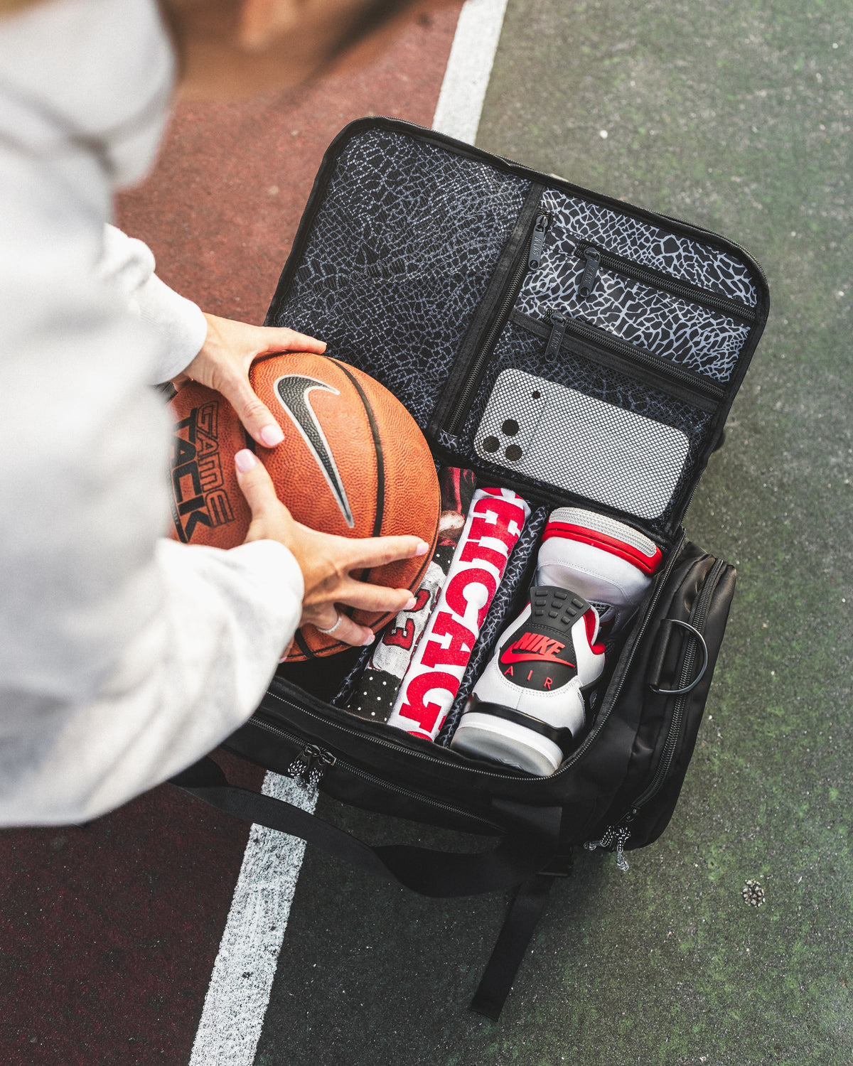 Open KXKS basketball gym bag showing a shoe compartment, folded tee and zip pockets in the grey print lining
