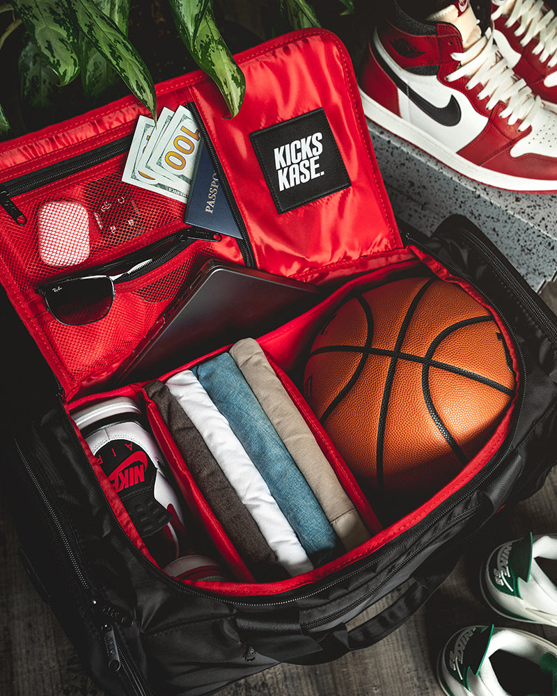 Open red travel case with basketball, clothes, and sunglasses, next to a pair of red sneakers.